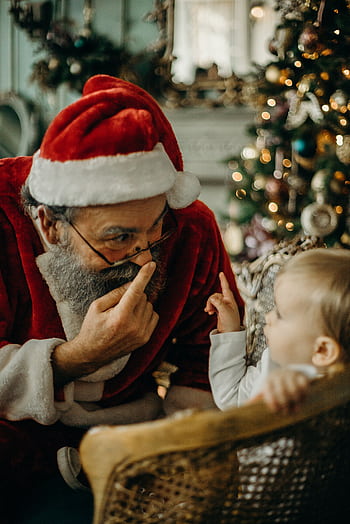 A child joyfully interacts with a Santa Claus figure beside a Christmas tree. HD phone wallpaper
