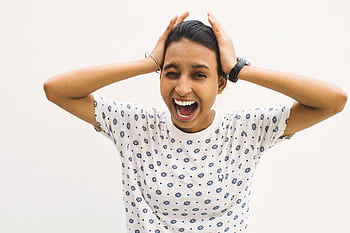 A young woman in a casual shirt screams with hands on her head against a white background. HD wallpaper