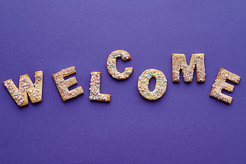 Colorful sprinkled cookies spelling 'welcome' on purple backdrop, perfect for celebrations. HD wallpaper