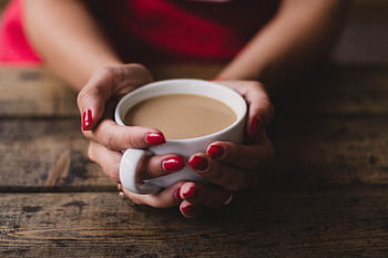 Warm indoor scene of a woman holding a steaming cup of coffee with red nails. HD wallpaper