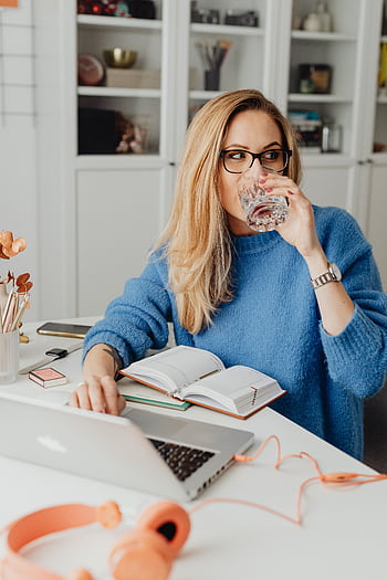 Blonde woman working from home with a laptop, notebook, and drink, embracing remote work lifestyle. HD phone wallpaper