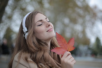Young woman with heads holding a red leaf, enjoying music outdoors in autumn. HD wallpaper