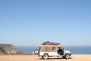 A jeep loaded with surfboards parked by a scenic ocean cliff under a clear sky. HD wallpaper