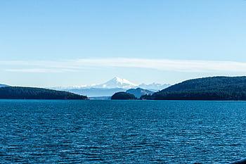 A stunning view of a blue ocean with a distant snow-capped mountain under a clear sky. HD wallpaper