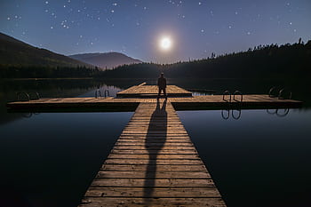 A man stands alone on a dock under a starry night sky in Whistler, BC, Canada. HD wallpaper