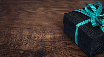A stylish black gift box with blue ribbon on a wooden table, perfect for celebrations. HD wallpaper