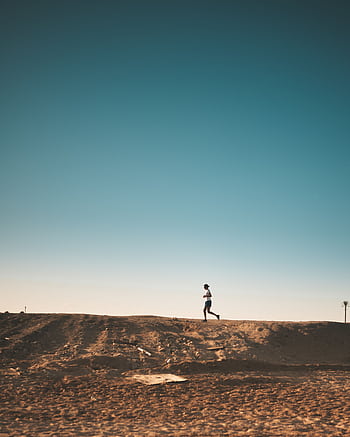 A person jogs on a sandy path with a vast blue sky above, capturing movement and dom. HD phone wallpaper