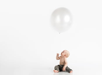 Cute baby holding a large balloon in a bright studio setup, reflecting innocence and joy. HD wallpaper
