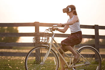 A teenager enjoys virtual reality while riding a bicycle outdoors at sunset. HD wallpaper