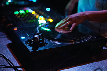 Close-up of DJ mixing on a turntable with colorful club lights, capturing vibrant nightlife atmosphere. HD wallpaper