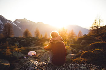 A woman sits on a rock enjoying the serene mountain view at sunrise in Sachseln, Switzerland. HD wallpaper