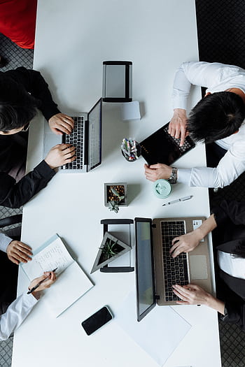 A diverse team working together in a modern office setting, focusing on laptops and collaboration. HD phone wallpaper
