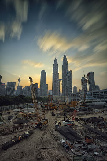 Dramatic view of the Petronas Towers towering over a busy construction site in Kuala Lumpur at sunset. HD phone wallpaper