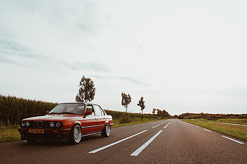 A classic red BMW sedan parked on a scenic countryside road during daylight. HD wallpaper