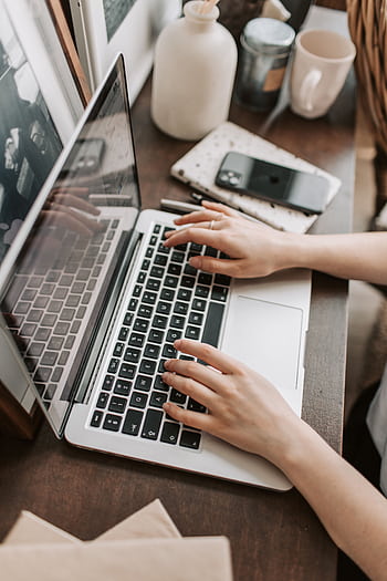 A woman is typing on a laptop at her desk, surrounded by personal items, illustrating a work-from-home setting. HD phone wallpaper