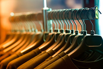 A row of neatly arranged clothes hanging on a rack with wooden hangers. HD wallpaper
