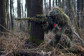 Sniper in camouflage gear taking aim in a dense forest environment. HD wallpaper