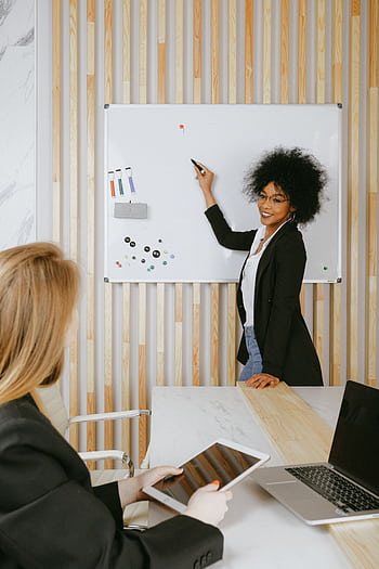 Confident businesswoman leading a presentation using a whiteboard in a modern office. HD phone wallpaper