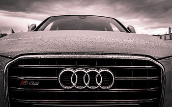 Close-up of a rain-covered Audi car grille showcasing luxury and elegance under cloudy skies. HD wallpaper