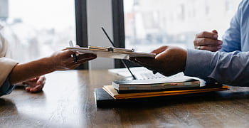 Hands exchanging documents during a professional meeting in an office environment. HD wallpaper