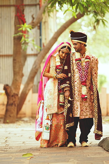 A joyful couple celebrates their traditional Indian wedding in vibrant outdoor attire. HD phone wallpaper