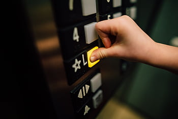 A close-up shot of a hand pushing the 'L' button in an elevator, indoors. HD wallpaper