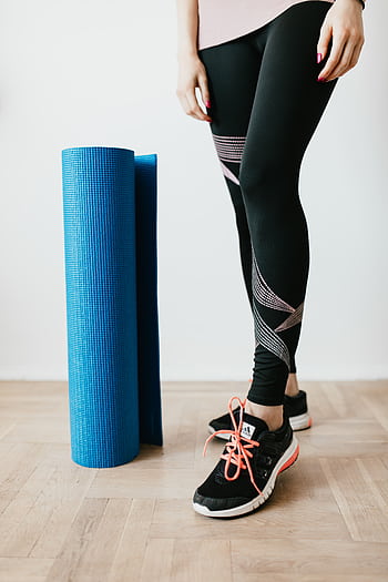 A woman in leggings and sneakers standing with a yoga mat indoors. HD phone wallpaper