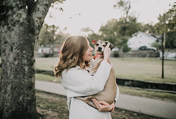 A joyful woman hugs her pet dog outdoors in a sunny park setting, showcasing affection and togetherness. HD wallpaper