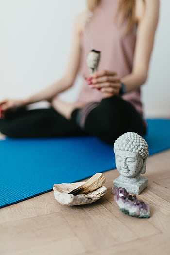 A serene yoga scene with a Buddha statue, amethyst crystal, and palo santo on a blue mat. HD phone wallpaper