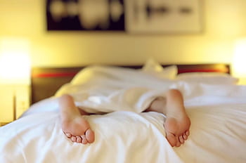 A person relaxing on a bed with feet under white sheets, conveying serenity. HD wallpaper