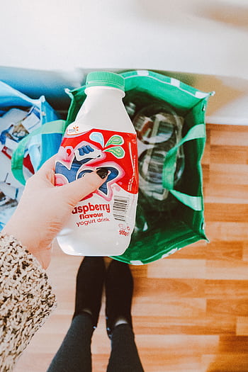 A person recycling a raspberry yogurt drink bottle into a green recycling bag. HD phone wallpaper
