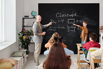 A teacher and students in a classroom during a geometry lesson, focused and engaging. HD wallpaper