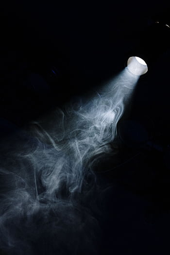 A beam of light penetrates through smoke in a dark setting, creating a moody atmosphere. HD phone wallpaper