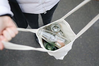 Person carrying a tote bag filled with glass bottles for recycling, promoting sustainability. HD wallpaper