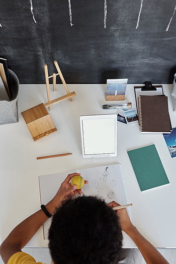 Overhead view of a teenager drawing at a desk with art supplies and tablet. HD phone wallpaper
