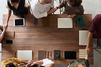 Group of adults having a business meeting, discussing plans around a wooden table with tech devices. HD wallpaper