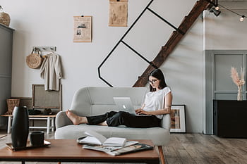 Young woman in modern living room comfortably working on laptop, embodying a relaxed and productive atmosphere. HD wallpaper