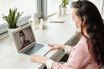 Woman and doctor video calling on laptop, both wearing masks, symbolizing telehealth during COVID-19. HD wallpaper