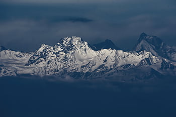 Breathtaking snow-covered mountains rising majestically under a moody sky, displaying nature's grandeur. HD wallpaper