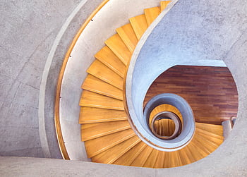 Aerial view of a stylish spiral staircase with wooden steps and a concrete interior. HD wallpaper