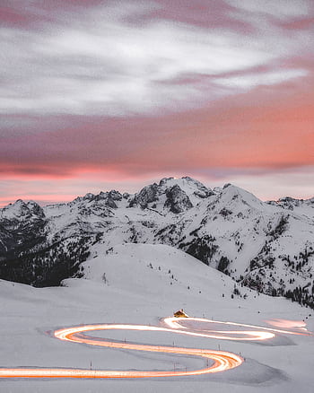 A winding road glowing under sunset skies amidst the snowy peaks of the Veneto Alps. HD phone wallpaper
