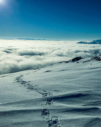 A breathtaking view of snowy mountains and footprints under a bright sky in Lenvik, Troms, Norway. HD phone wallpaper