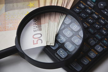 Euro bills under magnifying glass with calculator, symbolizing finance and analysis. HD wallpaper