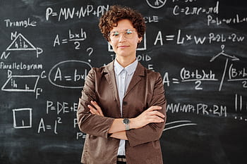 Confident female teacher standing with arms crossed in front of a detailed mathematical blackboard. HD wallpaper