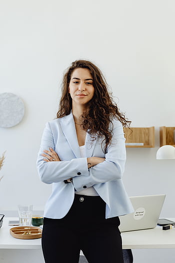 Professional woman in a white blazer standing confidently in an office with arms crossed. HD phone wallpaper