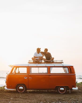 Two friends sit on a vintage van's roof at sunset by the sea, enjoying a tranquil moment. HD phone wallpaper