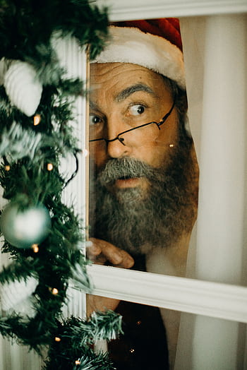 A bearded man dressed as Santa Claus peeking through a decorated window indoors. HD phone wallpaper