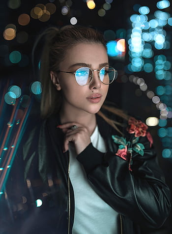 Fashionable woman in glasses and black jacket with city bokeh lights at night. HD phone wallpaper
