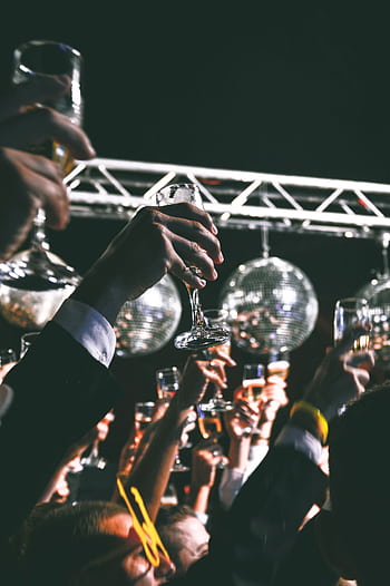 A festive gathering with people raising glasses in a toast under shiny disco balls at a night event. HD phone wallpaper
