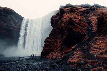 A group of adventurers stands before the majestic Skogafoss waterfall in Iceland. HD wallpaper
